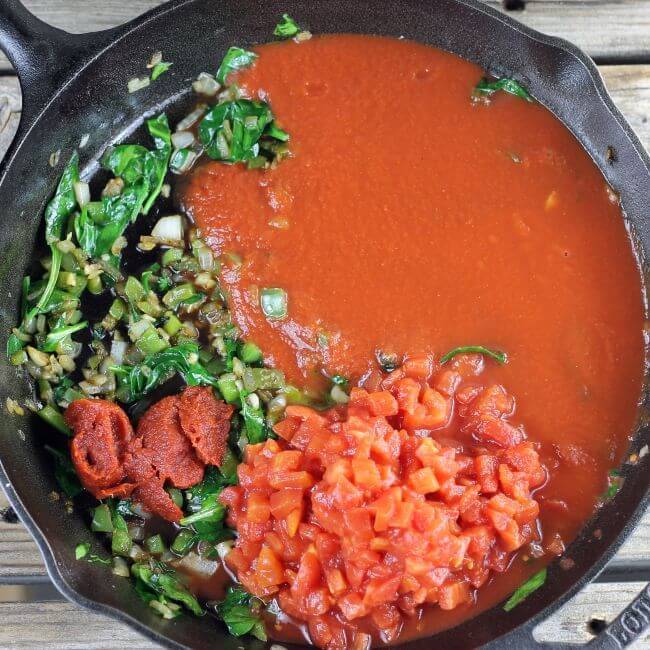 Tomato sauce, diced tomatoes, and past is added to the vegetables in the skillet.