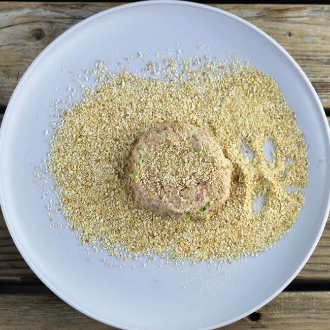 Coating a tuna cake with bread crumbs on a gray plate.
