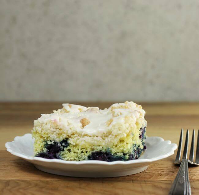 Side view of lemon blueberry coffee cake on a white plate.