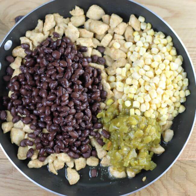 Black beans, chiles, and corn are added to the chicken in the skillet.