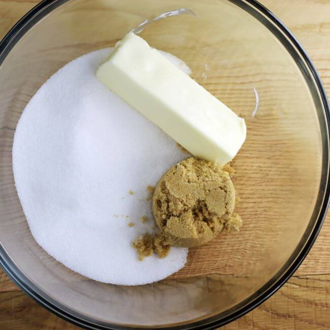 Butter, brown sugar, and sugar are added to a glass bowl.