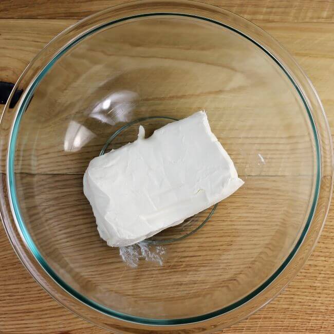 A block of cream cheese in a glass bowl.