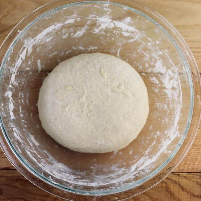 Pizza crust dough in a glass bowl.
