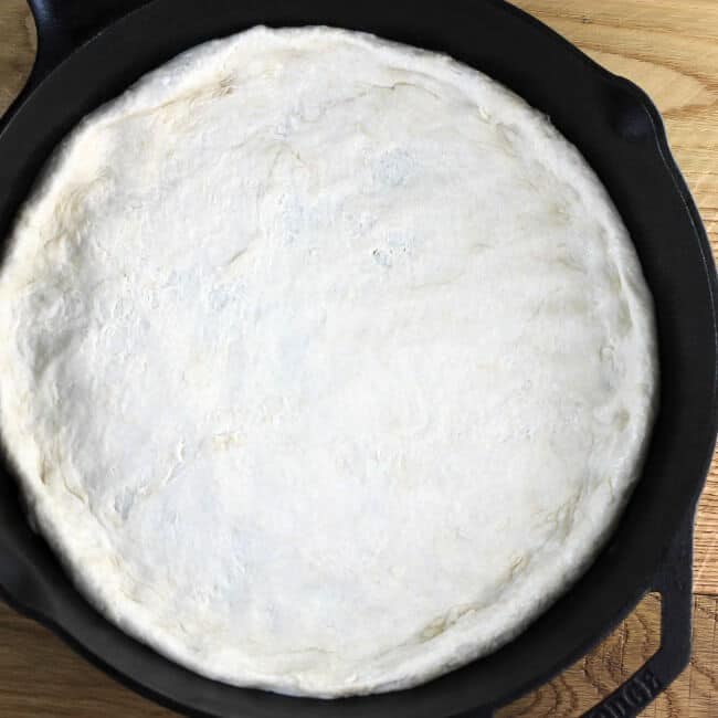 Pizza dough is spread out for the crust in a skillet