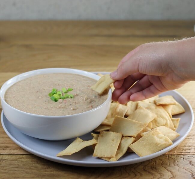 A side view of someone with a cracker taking some dip from a bowl of bean dip.