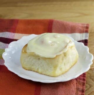 Side angle view of a orange sweet roll on a white plate.