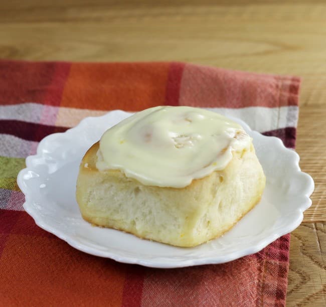 Side angle view of a orange sweet roll on a white plate.
