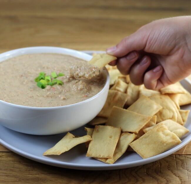 Some lifting a cracker with dip on the cracker.