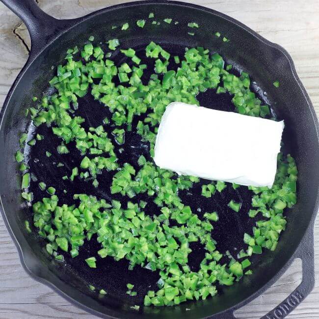 Cream cheese is added to the jalapenos in the skillet.