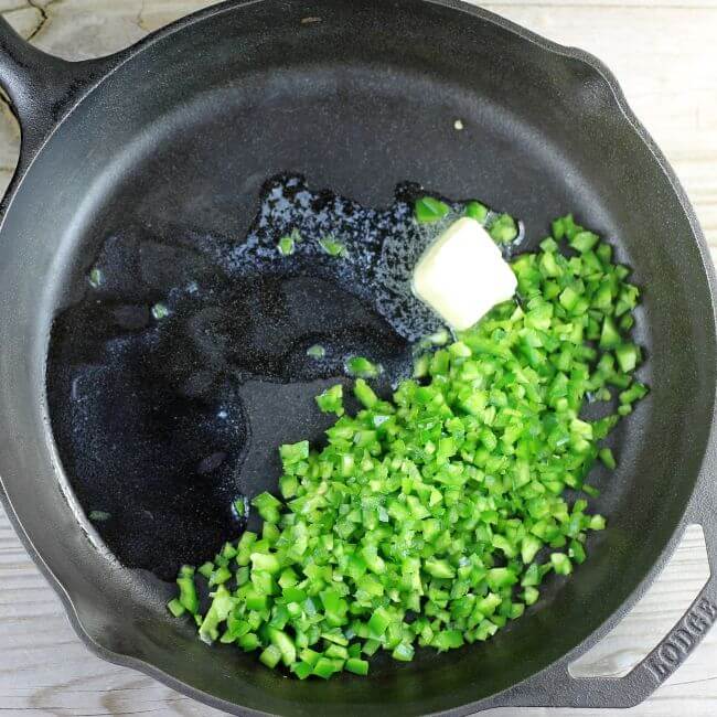 A skillet with butter and minced jalapenos in it.