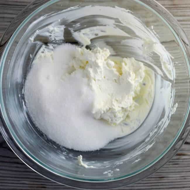 Sugar is added to the cream cheese in the bowl.