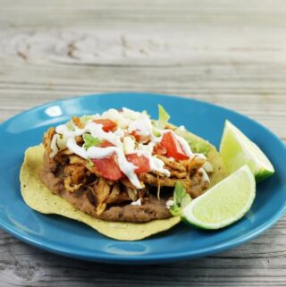 Looking at a side view of a blue plate with a tostada loaded with toppings.