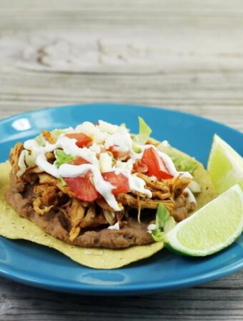 Looking at a side view of a blue plate with a tostada loaded with toppings.