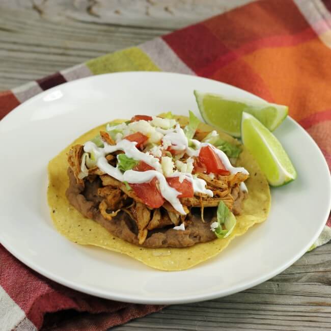 Side angle view of a white plate with a chicken tostada on it.