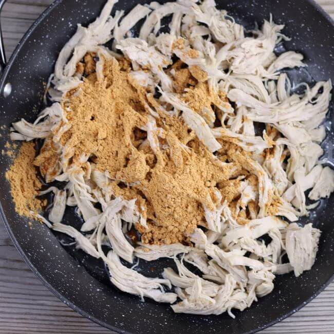 Taco seasoning, water, and shredded chicken in a skillet.
