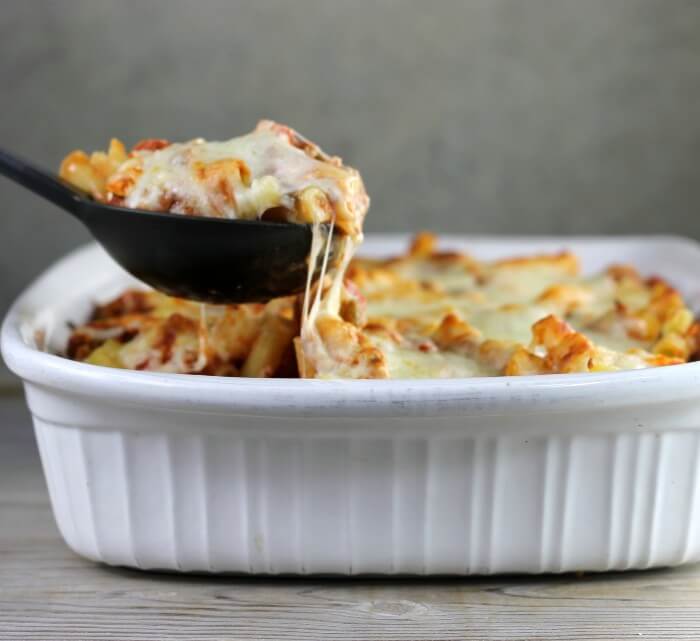 Taking a scoop of baked ziti out of baking dish.