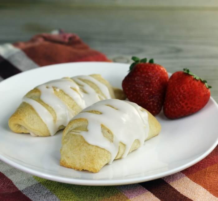 A side view of two crescent rolls with strawberries on a white plate. 