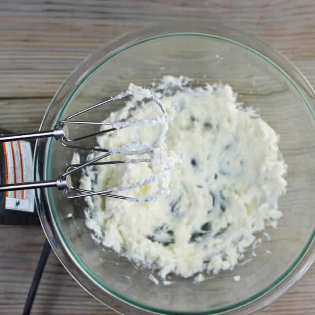 Cream cheese is beaten with an electric mixer in a medium bowl.