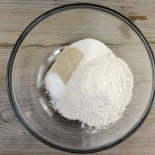 Flour, yeast, sugar, and salt are added to a bowl.