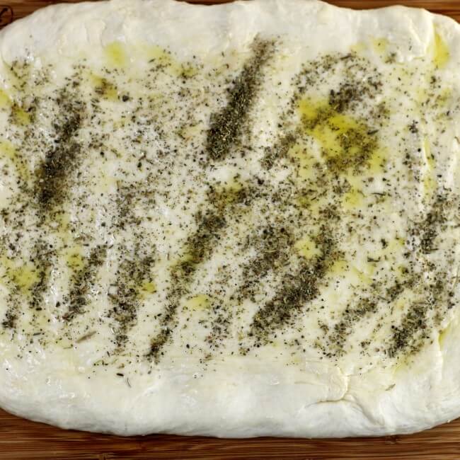 Italian seasoning is sprinkled over top of the pizza dough.
