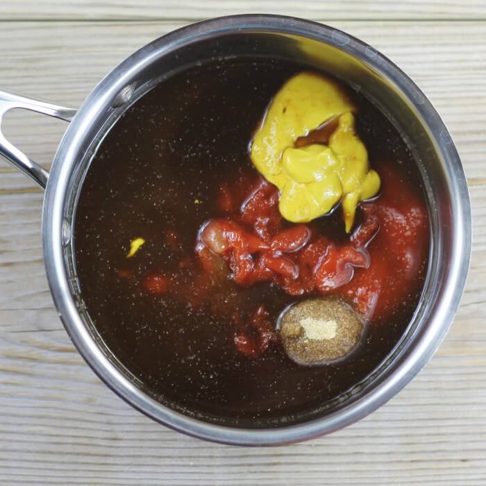 Looking down at a saucepan that has ketchup, mustard, brown sugar, Worcestershire sauce, onion powder, and vinegar in ti.