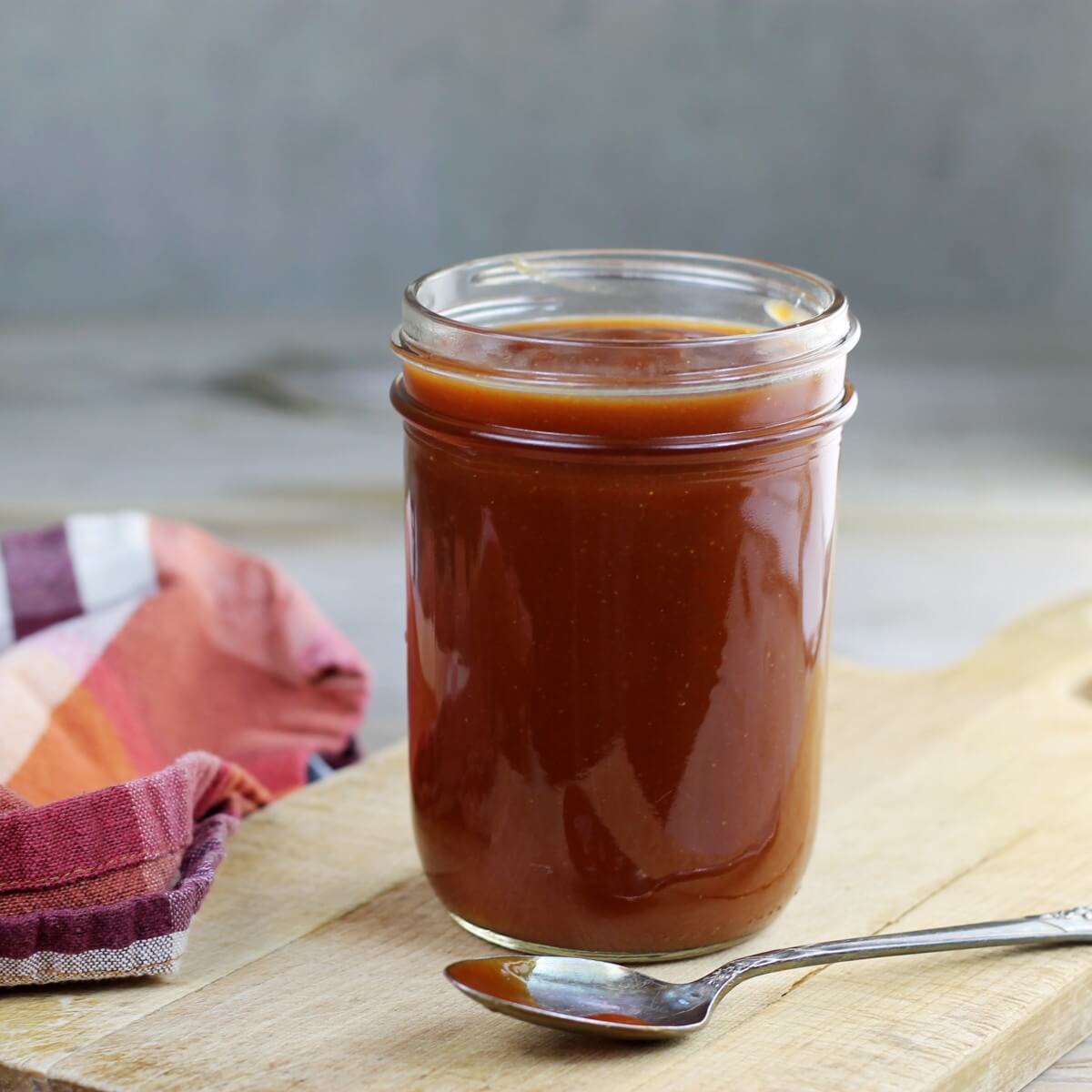 A jar filled with BBQ sauce with a spoon set in front of it.
