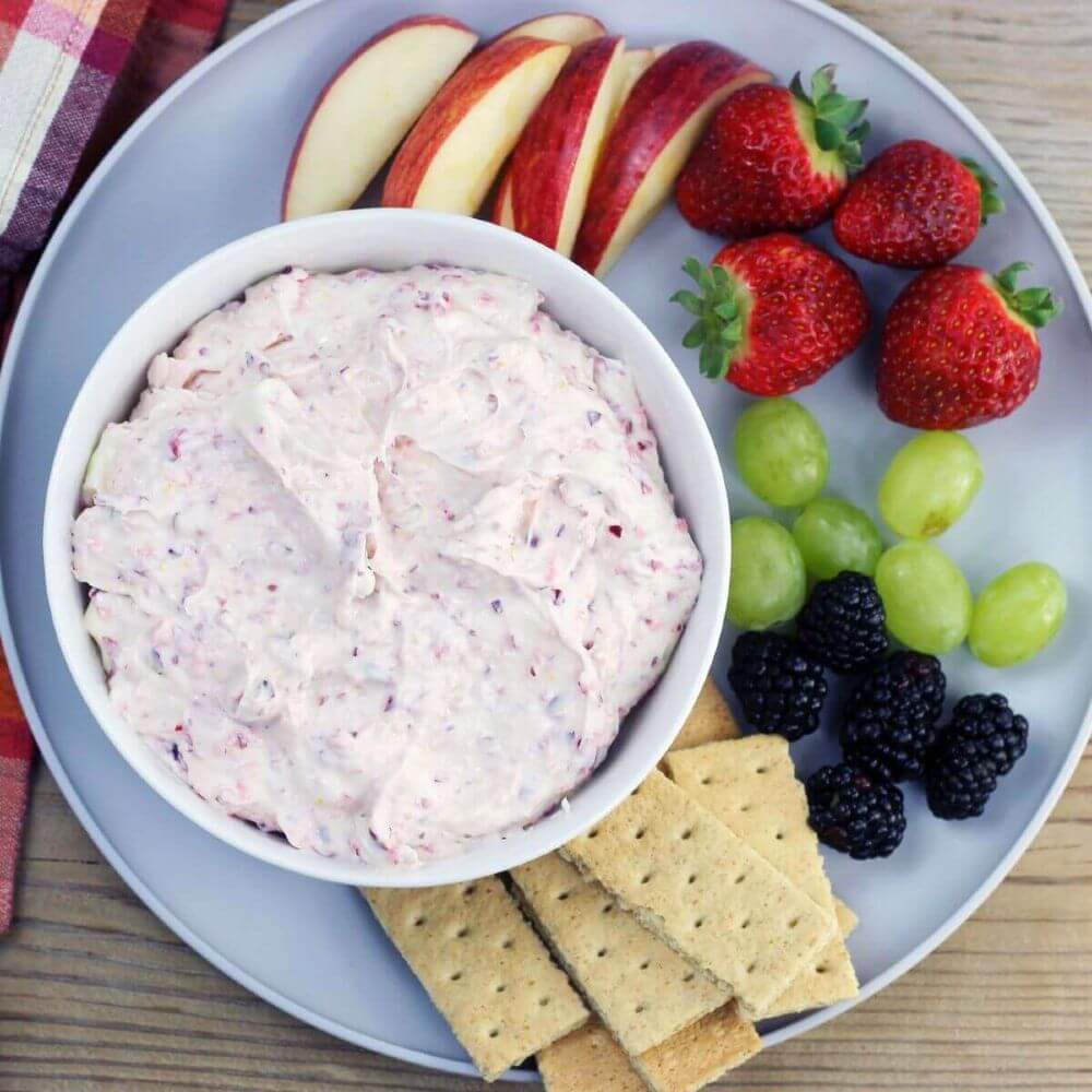 Looking down at a plate with fruit, graham crackers, and a bowl of dip. 