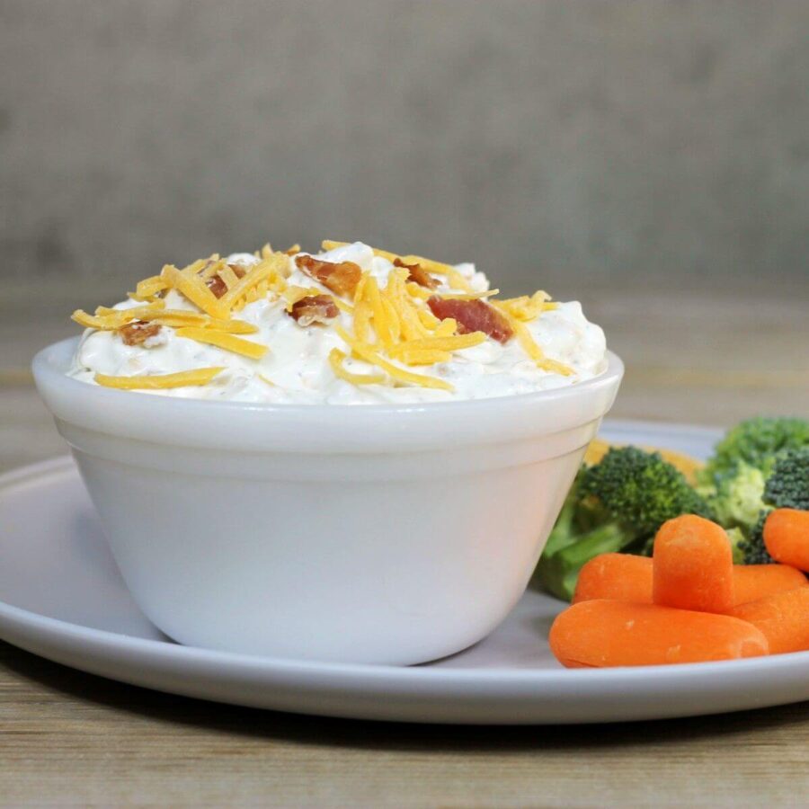 A side view of a bowl of dip on a plate with veggies.