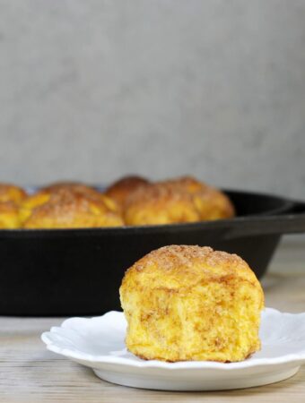 A side view of a pumpkin roll on a plate in front of a skillet.