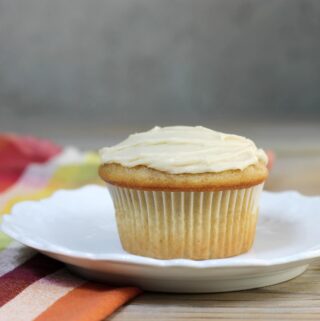 A side view of a white plate with an frosted apple cupcake on it.