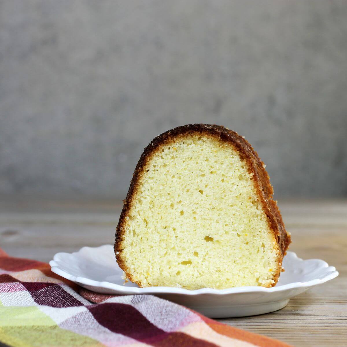 A side view of a slice of cake on a white plate with a napking on the side.