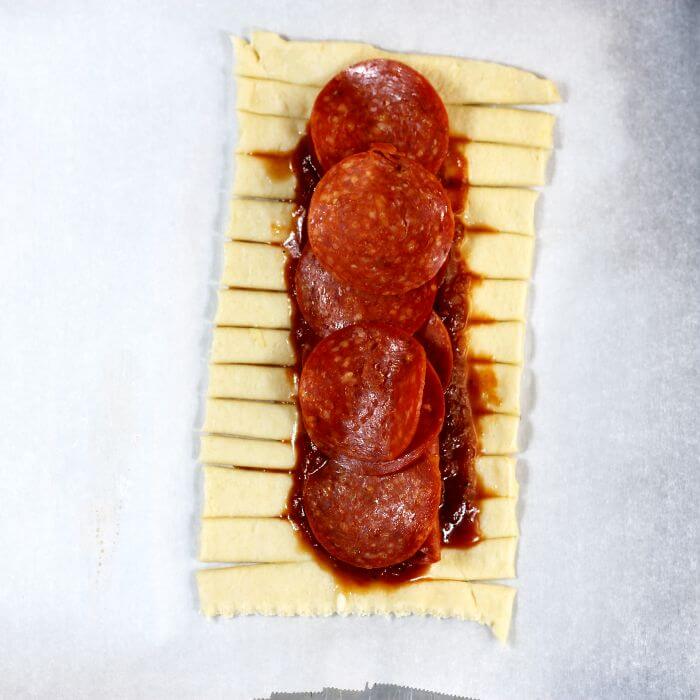 Pepperoni slices are placed on top of the pizza sauce.