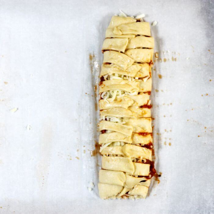 The strips of dough are pulled over top of the pizza toppings.